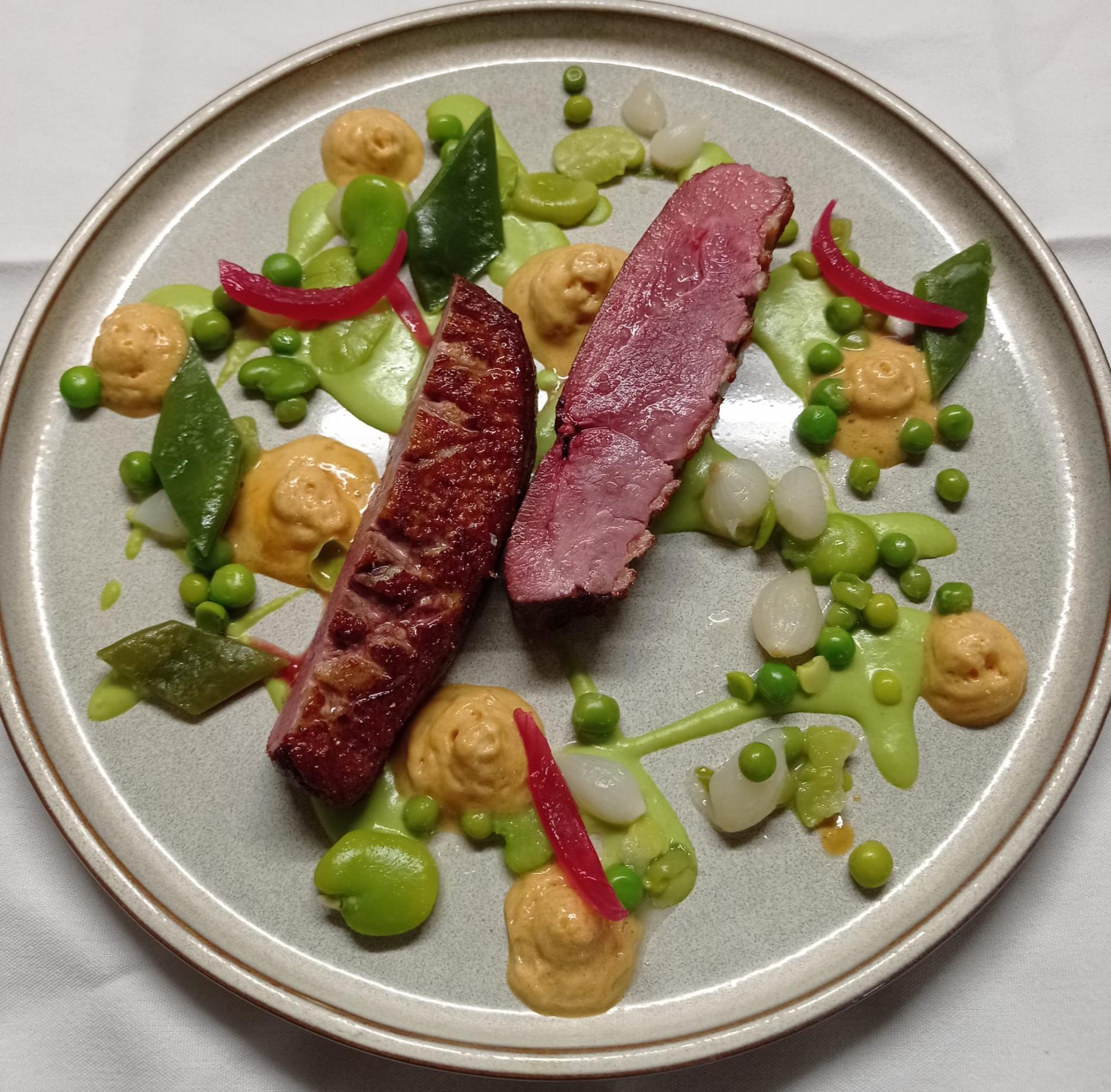 - Filet de canette rôti, mousseline de petits pois, étuvée de fèves et haricots plats, crème d’oignons.